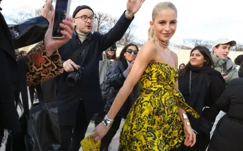 Mujer con un llamativo vestido globo amarillo y negro, rodeada de gente y fotógrafos.