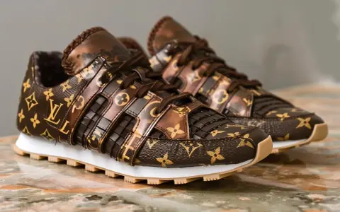 Brązowe buty sportowe Louis Vuitton z monogramem na marmurowym tle.