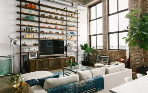 Soggiorno con scaffalatura a tutta parete, TV e divano bianco. Il soffitto alto 5 metri crea un'atmosfera ariosa, accentuata dalle grandi finestre.