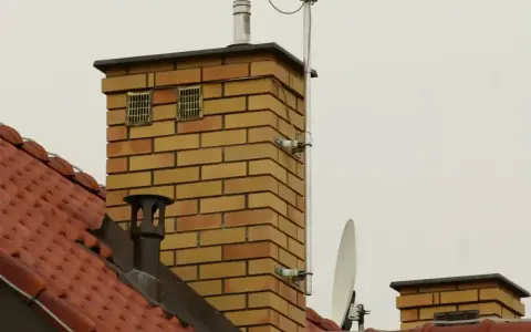 Dwa kratkowane otwory wentylacyjne na ceglanym kominie, zapewniające prawidłowe odpowietrzenie pionu sanitarnego zgodnie z normą.