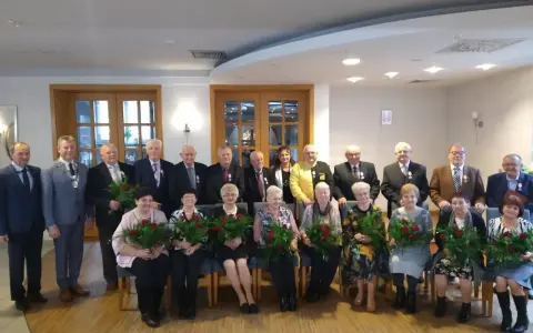 Grupa osób świętuje 50 rocznicę ślubu. Wszyscy otrzymują róże i medale.