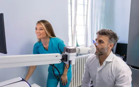Mann macht Lungenfunktionstest, Arztin überwacht. Ergebnisse zeigen 70 Prozent Lungenfunktion.