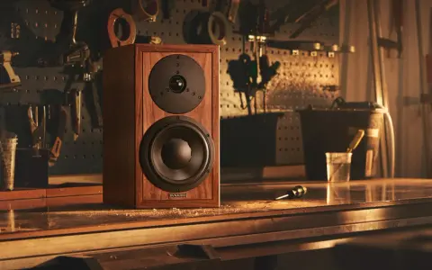 Głośnik Dynaudio Special 25 w drewnianej obudowie, stojący na stole w warsztacie, otoczony narzędziami.