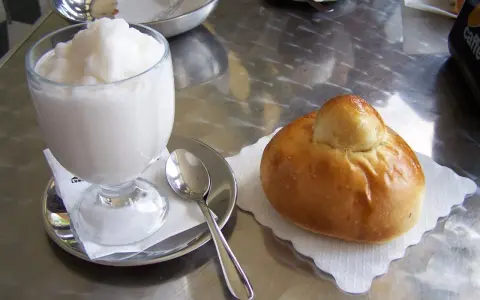 Un bicchiere di granita bianca e un soffice brioche col tuppo su un tavolo metallico.
