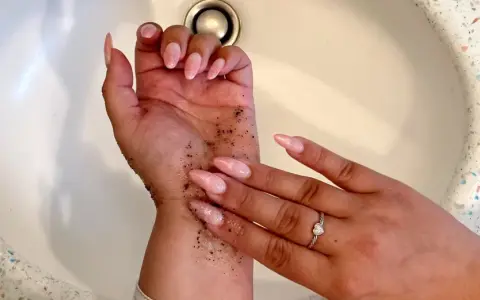 Manos con uñas largas y rosadas, cubiertas de gránulos oscuros. Parece un autobronceador mal aplicado que se está intentando lavar.