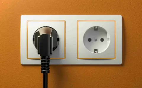 Dwa gniazdka elektryczne, jedno z wtyczką, na pomarańczowej ścianie. Typowe gniazdka w Hiszpanii.