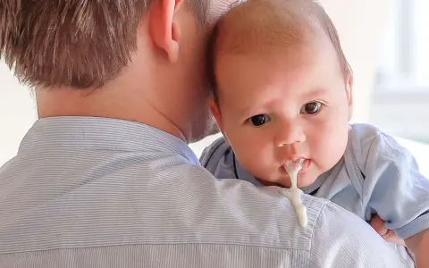 Un padre tiene in braccio il suo neonato, che ha un rigurgito visibile.