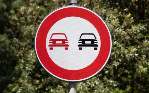 Segnale stradale art. 148: divieto di sorpasso per autoveicoli. Due auto stilizzate, una rossa e una nera, su sfondo bianco e bordo rosso.