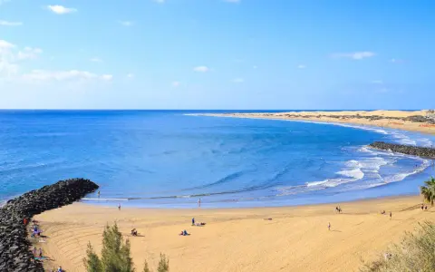 Sonniger Strand auf Gran Canaria mit goldenem Sand, türkisfarbenem Meer und einigen Menschen, die die Sonne genießen.