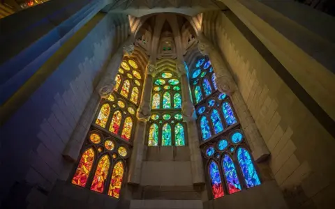 Ventanas de vidrieras de colores vibrantes, que narran la historia del vidrio, iluminan el interior de una catedral con tonos cálidos y fríos.