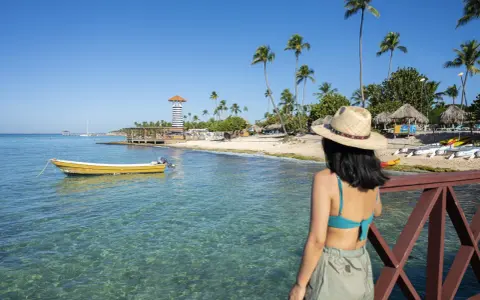 Kobieta w kapeluszu podziwia plażę z latarnią i palmami. Czy to Puerto Plata czy Punta Cana?