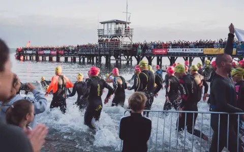 Triathleten starten ins Wasser, die Menge jubelt vom Steg. Die Ironman Vorbereitung ist in vollem Gange.