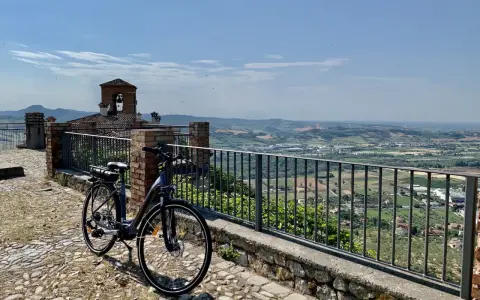 Bicicletta pronta per esplorare il **percorso fiume Marecchia**, con vista panoramica sulla valle e un antico campanile.