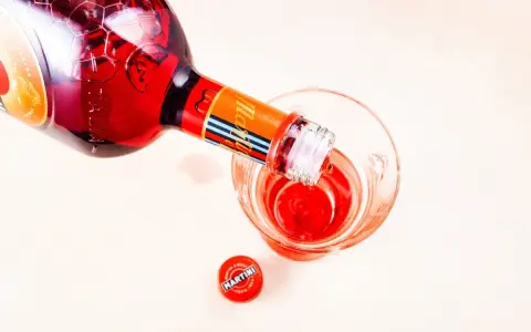 Czerwony Martini Fierro nalewany do kieliszka. Obok leży czerwona zakrętka z logo Martini.