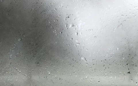 Gotas de agua sobre un cristal, reflejando un cielo nublado. La **temperatura de rocío** se siente en el aire húmedo.