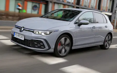 Szary Volkswagen Golf GTE porusza się po miejskiej drodze, z rozmytym tłem budynków i przechodniów.