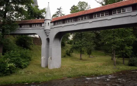 Mostek z wieżyczką, jedna z atrakcji Lądka Zdroju, przerzucony nad strumieniem, otoczony zielenią.