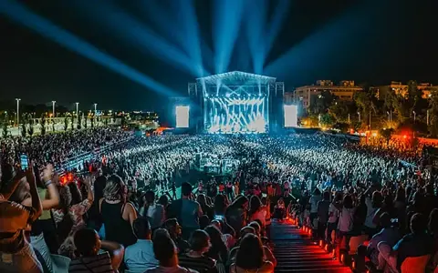 Gran concierto nocturno con multitud de público frente a un escenario iluminado con luces azules.