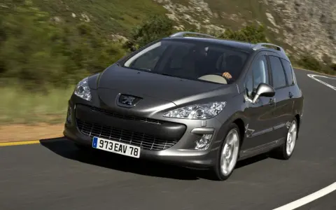 Szary Peugeot 308 2008 na krętej drodze wśród zielonych wzgórz.