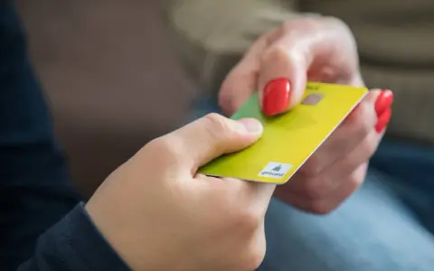 Eine Hand gibt einer anderen eine gelbe Girocard. Dies könnte die erste kinder debitkarte sein, die ein Kind erhält.