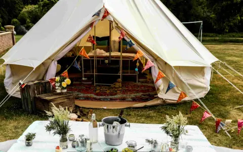 Idealne miejsce na glamping: namiot typu bell z kolorowymi chorągiewkami, stół z winem i kwiatami.