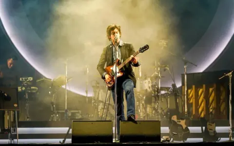 Alex Turner z Arctic Monkeys Polska na scenie, grając na gitarze w otoczeniu dymu i świateł.