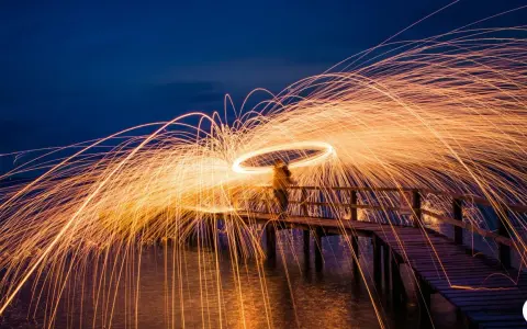 Une personne sur un pont crée une **light painting photo** spectaculaire avec des traînées de feu dans le ciel nocturne.