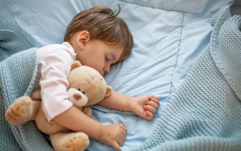 Małe dziecko śpi z misiem. Nadmierna senność u niemowlaka może mieć różne przyczyny, ale ten maluch wygląda na spokojnego.