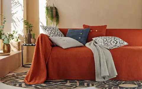 Un canapé ancien relooké en orange vif, orné de coussins graphiques et d'une couverture grise. Une touche bohème moderne.
