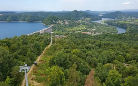 Widok na zielone wzgórza nad Soliną, z widoczną zaporą, jeziorem i kolejką gondolową. Trasa widokowa zachwyca.