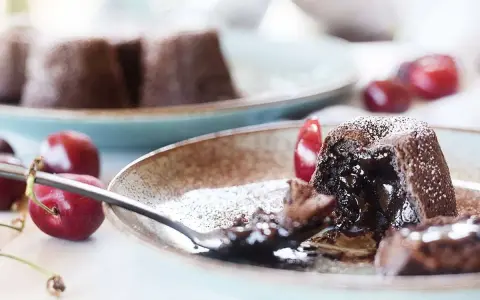 Coulant de chocolate con interior fundido, espolvoreado con azúcar glas y acompañado de cerezas frescas.