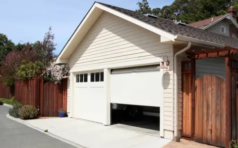 Jasny garaż murowany bez pozwolenia, z częściowo otwartą bramą, obok drewnianego ogrodzenia i bramy.