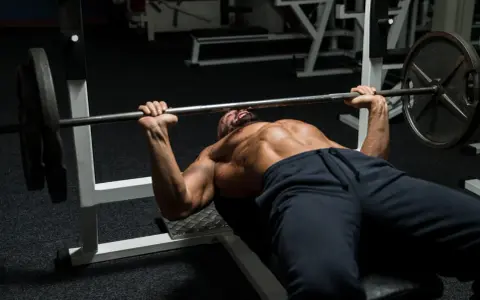 Man med skägg och synliga muskler utför bänkpress som en del av sitt starting strength program.