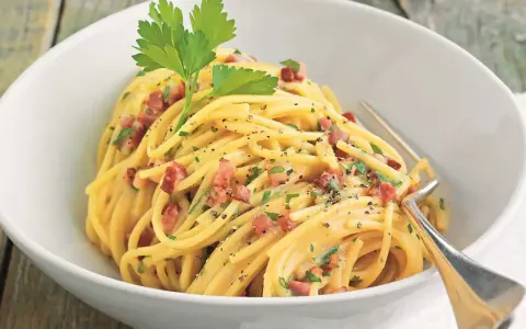 Spaghetti Carbonara mit knusprigem Schinken, garniert mit Petersilie und schwarzem Pfeffer, serviert in einer weißen Schüssel.