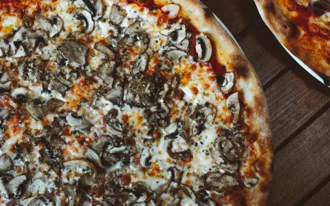 Pyszna pizza wegetariańska z pieczarkami i ciągnącym się serem, idealna na wspólny wieczór.