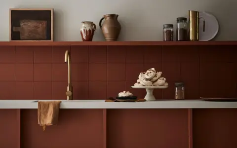 Encimera de cocina pintada en tono terracota, con grifería dorada y detalles decorativos.