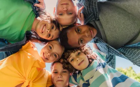 Un groupe d'enfants souriants forme un cercle, leurs visages se rejoignant au centre. Leurs regards joyeux et leurs expressions témoignent d'un bel encadrement d'enfants.