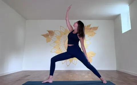 Kvinna i krigarställning i ett ljust rum med solrosmålning på väggen. En lugn yoga andrum.