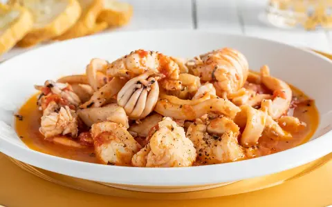Un invitante piatto di zuppa di pesce, ricco di calamari, gamberi e pesce bianco, servito con crostini dorati.