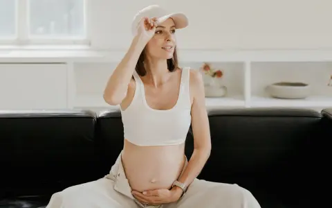Kobieta w ciąży, czując uderzenia gorąca, poprawia czapkę. Siedzi na czarnej kanapie w jasnym wnętrzu.