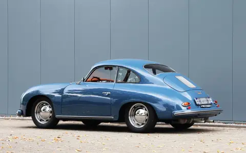 Blauer Porsche 1600 Super Coupé, ein Klassiker mit hohem Wert, steht vor einer grauen Wand.