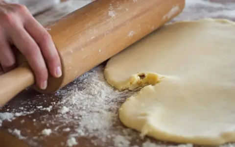 Mains roulant une pâte à biscuits trop sableux. Farine saupoudrée sur la planche en bois.