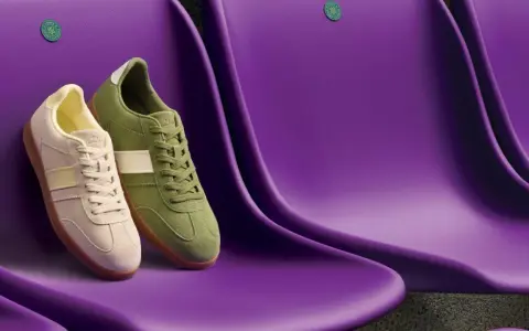 Due sneakers Clarks, una beige e una verde, sedute su sedili viola. Le Clarks calzano mezza misura in meno, perfette per un look casual.