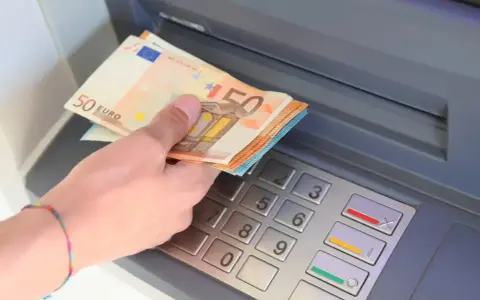 Dłoń trzyma banknoty 50 euro przy bankomacie. W Hiszpanii, jak w całej strefie euro, obowiązuje euro.