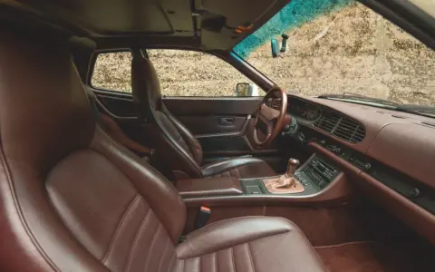 Das **Porsche 944 Interieur** mit braunen Ledersitzen und Armaturenbrett. Ein Blick auf das Lenkrad, den Schalthebel und das Radio.