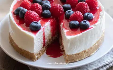 Delizioso cheesecake con mascarpone, guarnito con lamponi freschi, mirtilli e una cascata di salsa rossa.