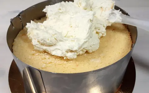 Nakładanie puszystego kremu mascarpone na biszkopt w tortownicy.