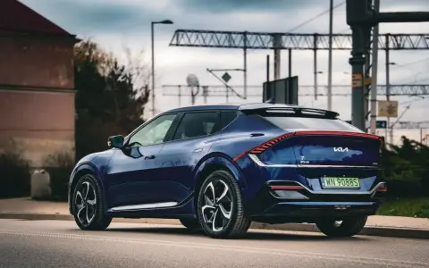 Granatowe Kia EV6 GT z charakterystycznym pasem świateł z tyłu, zaparkowane przy drodze z widoczną infrastrukturą kolejową.