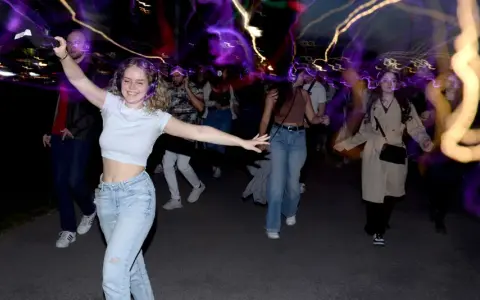 Junge Leute mit Kopfhörern, die im Dunkeln tanzen gehen, umgeben von bunten Lichtspuren.
