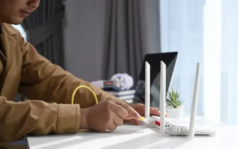 Mann schließt ein Netzwerkkabel an einen Router an, um seinen Laptop als Router zu verwenden.